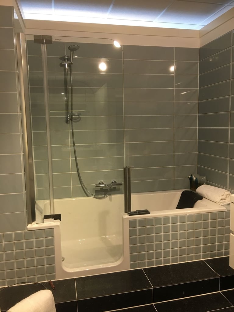 Modern bathroom with gray subway tile walls, walk-in shower with glass enclosure, white soaking tub, and recessed lighting